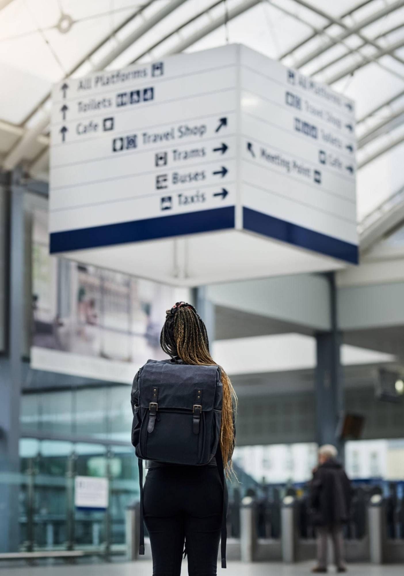 Traveller with a backpack looking up at directional signs in a station hall