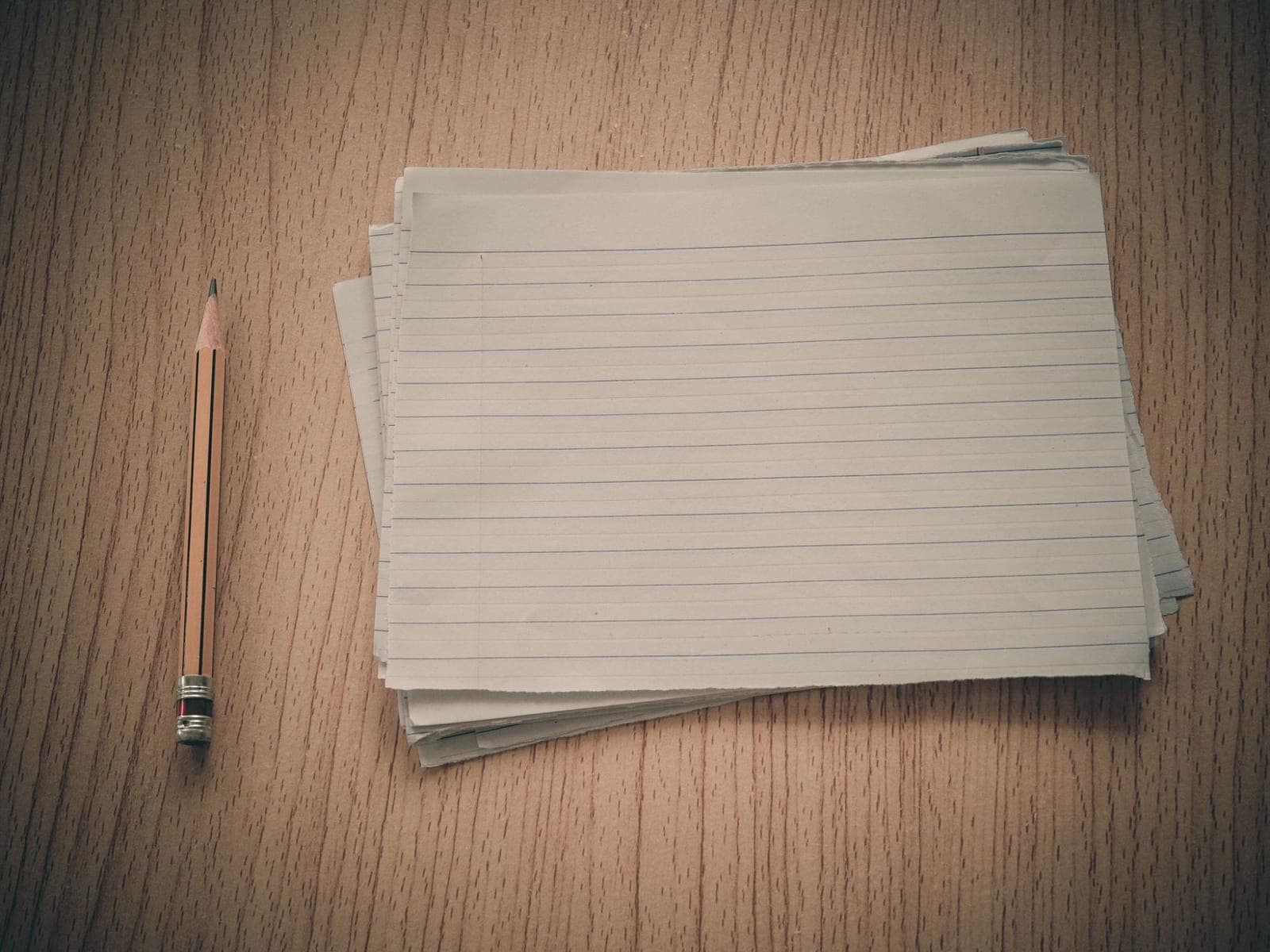 A stack of ruled cards beside a pencil on a wooden table