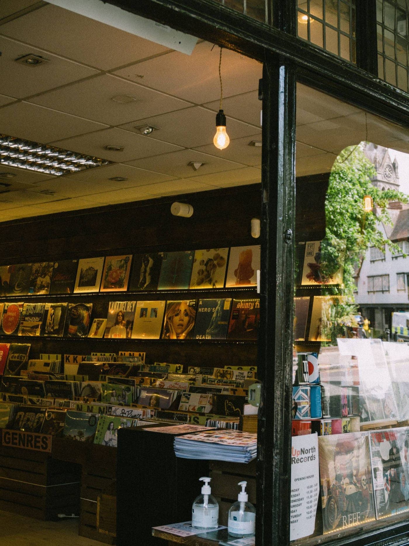 Record shop seen through an open shopfront, with shelves of records, a hanging bulb and a window onto the street